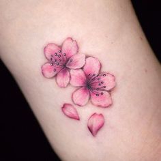 a small pink flower tattoo on the left side of the leg, with black dots