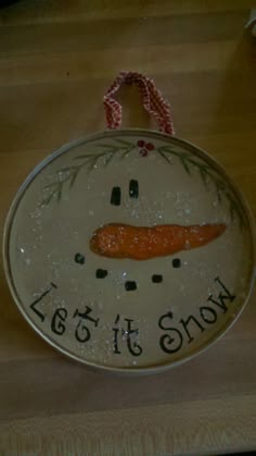 a snowman ornament hanging on a wooden table with the words let it snow