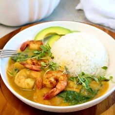 a white bowl filled with shrimp, rice and avocado on top of a wooden table