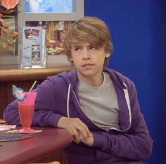 a boy sitting at a table with a drink