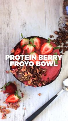 a bowl filled with strawberries and granola next to a spoon on top of a table