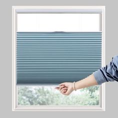 a woman is looking out the window with her hand on the blinds and pointing at it