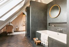 an attic bathroom with wood flooring and gray walls, along with a white bathtub