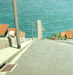 an empty street next to the ocean with houses on either side and water in the background