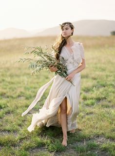 a woman in a white dress is holding a plant and wearing a wreath on her head