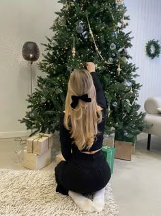 a woman sitting on the floor in front of a christmas tree