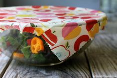 a glass bowl filled with vegetables on top of a wooden table covered in a colorful cloth