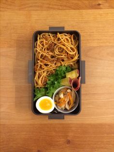 a lunch box with noodles, meats and vegetables in it on a wooden table