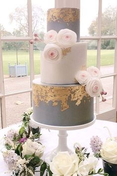 a three tiered cake sitting on top of a table next to white and pink flowers