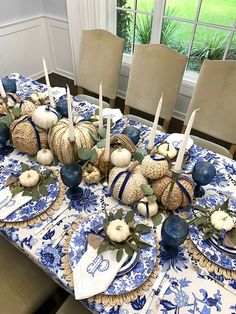 the table is set with blue and white dishes, pumpkins and candlesticks