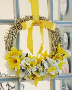 a wreath with yellow and white flowers hanging from the front door, decorated with ribbon