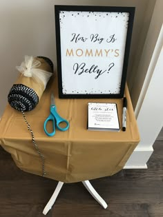 a table with a sign and scissors on it next to a box that says, how big is mommy's belly?