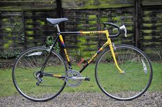 a yellow and black bike parked on top of a gravel road next to a wooden fence