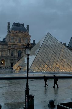 two people walking in front of a large glass pyramid