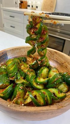 a wooden bowl filled with green peppers on top of a white counter next to a stove