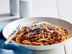 a white bowl filled with spaghetti and sauce on top of a blue towel next to a cup