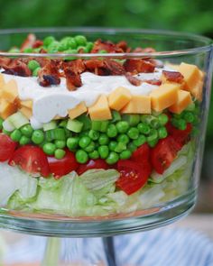 a salad in a glass bowl with bacon, lettuce and cheese on top