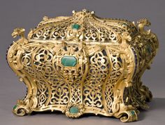 an ornately decorated gold box with green and blue stones on the front, sitting against a gray background