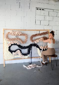 a woman sitting on a chair next to a large piece of art made out of yarn