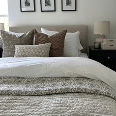 a bed with white sheets and pillows in a bedroom next to two framed pictures on the wall