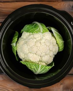 a head of cauliflower in a black crock pot on a wooden table