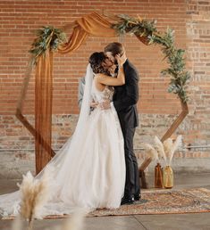 a bride and groom kissing in front of an arch decorated with greenery