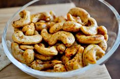 a glass bowl filled with cashews on top of a wooden cutting board