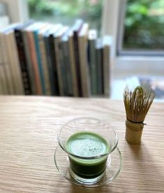 a cup of green tea next to a bamboo stick on a wooden table with books in the background