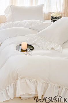 a white bed with ruffles and a candle on the end table in front of it