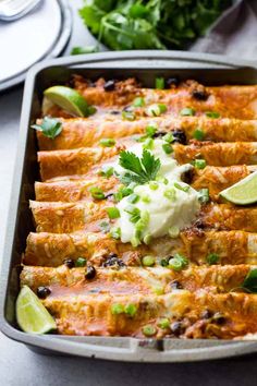 mexican enchiladas in a baking pan with sour cream and cilantro