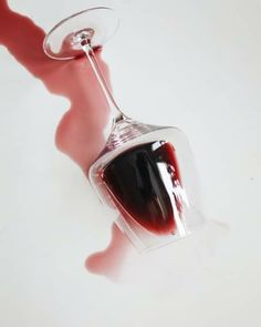 a wine glass filled with red liquid sitting on top of a white table next to a person's leg