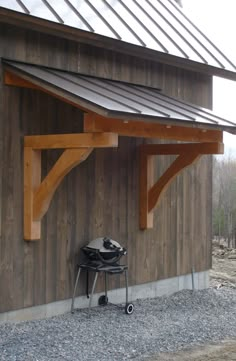 a grill sits under a wooden structure on the side of a building with a metal roof