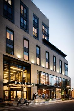 the exterior of a hotel at dusk with people sitting outside and on motorcycles parked in front