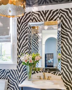 a bathroom with zebra print wallpaper and white sink, gold lights above the mirror