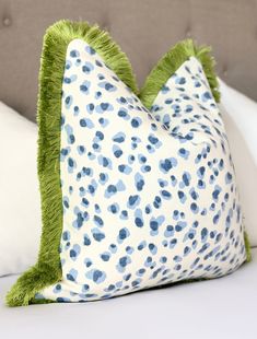 a blue and white leopard print pillow with green fringe on the bottom, sitting on a bed