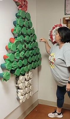 a pregnant woman pointing at a christmas tree made out of cans