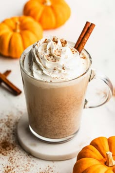 a cup of hot chocolate topped with whipped cream and cinnamon sticks next to mini pumpkins