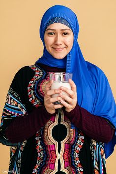 a woman wearing a blue head scarf and holding a glass in her hands with a smile on her face