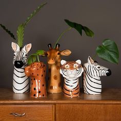 three ceramic zebras and two giraffes are on a dresser