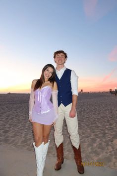 a man and woman standing on top of a sandy beach next to the ocean at sunset