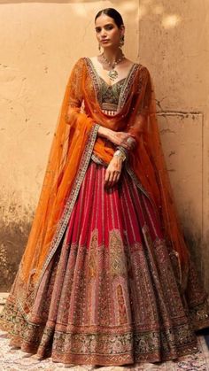 a woman in an orange and red lehenga standing next to a white wall