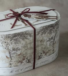 a white box with a red ribbon tied around it and an ornate design on the lid