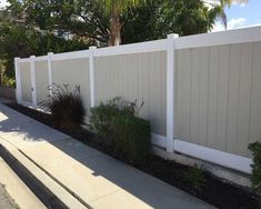 a white picket fence with plants growing on the side