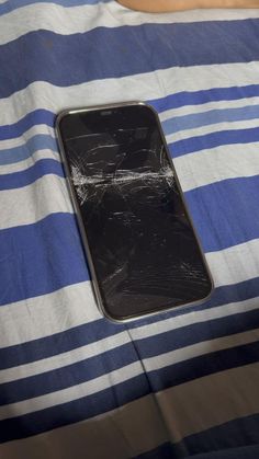 a broken cell phone laying on top of a blue and white striped bed sheet,