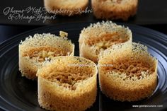 four small cakes on a black plate with white sprinkles and some sort of powdered sugar