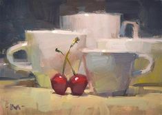 two cherries sit on a table next to cups