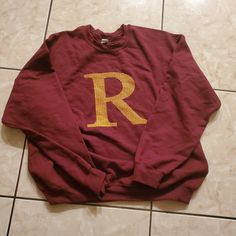 a maroon sweatshirt with the letter r on it sitting on a tile floor in front of a tiled wall