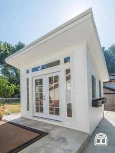 a small white house sitting on top of a cement floor next to a fenced in yard