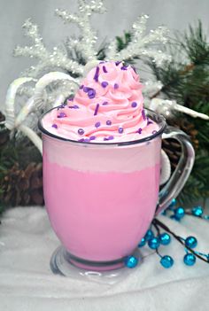 a pink frosted drink with sprinkles in a glass mug next to christmas decorations