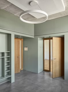 an empty room with two open doors and shelves on the wall, in front of a circular light fixture